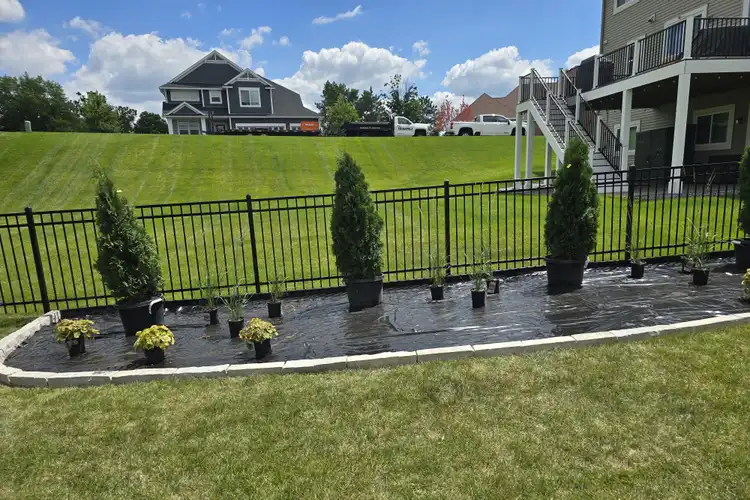 Arborvitae and annual shrubs staged for planting along residential fence line