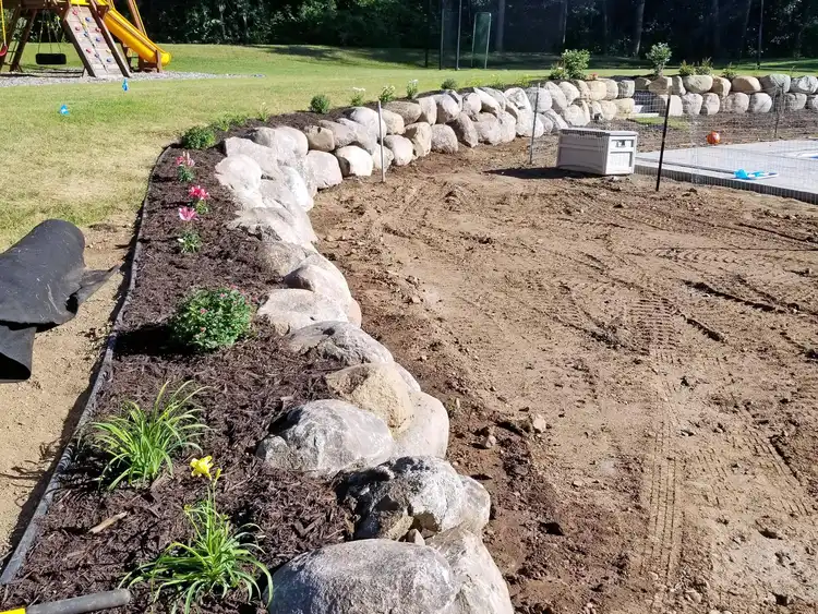 Boulder retaining wall installation along curved backyard landscape bed