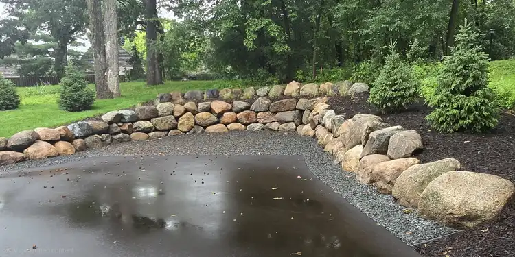 Boulder fieldstone retaining wall curving around driveway with landscape bed