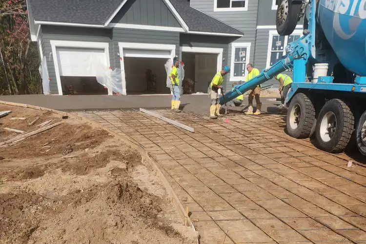 Concrete driveway pour with rebar grid and crew finishing at new construction home