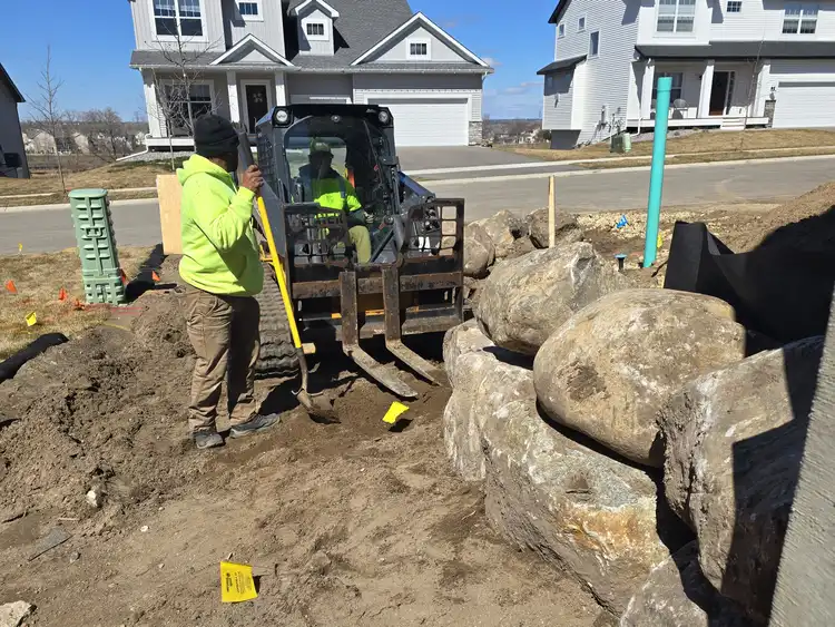 Skid steer placing large boulders at residential job site
