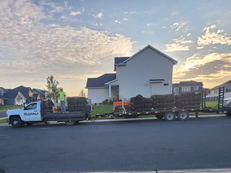 Ristau flatbed trailer loaded with sod rolls at residential property at dawn