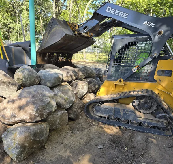 John Deere skid steer placing boulders for retaining wall installation