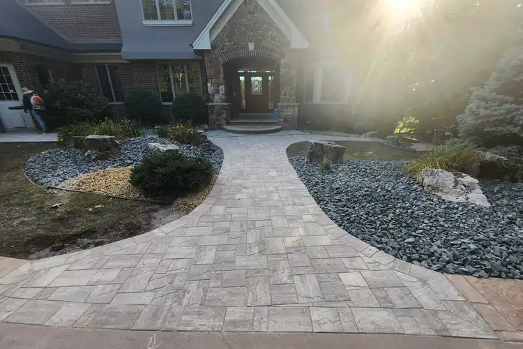 Paver walkway leading to residential front entry with landscape beds at sunset