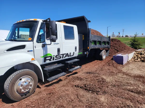 Ristau branded dump truck delivering bulk mulch to commercial job site