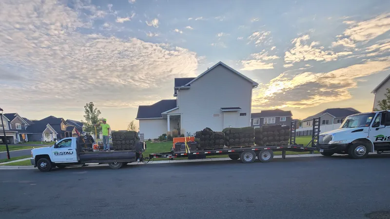 Ristau truck and trailer delivering sod pallets in residential neighborhood at dawn